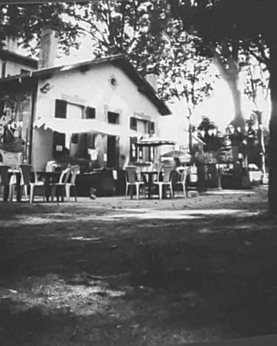 Tirage argentique noir et blanc d'une guinguette sous les arbres, tables et chaises en terrasse